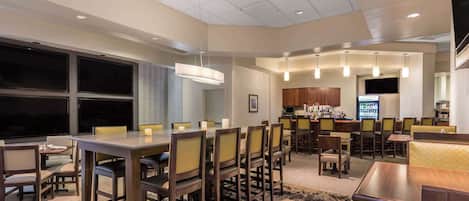 A modern dining area with multiple tables and chairs, a bar area with a counter and stools, and a kitchen in the background.