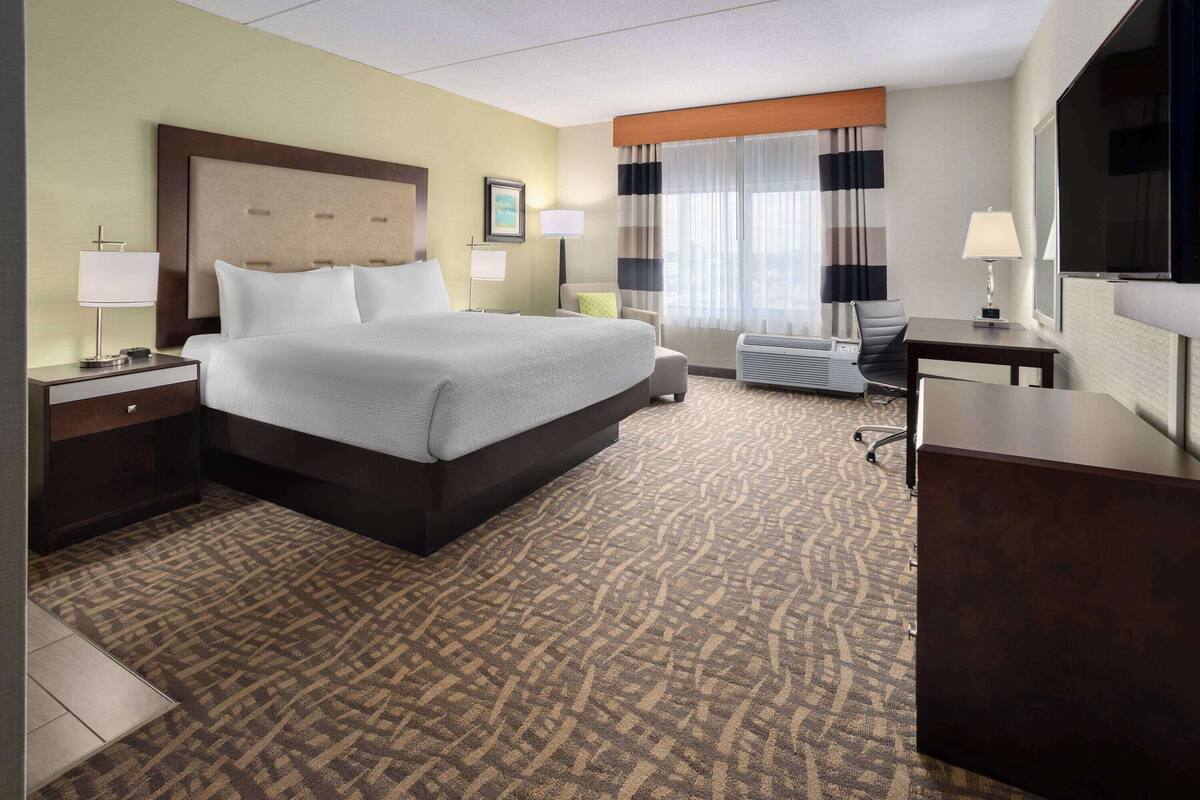 Une chambre d’hôtel avec un grand lit, un bureau, une chaise, une télévision et une fenêtre avec des rideaux.