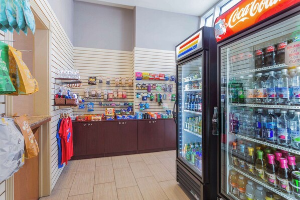 Un refrigerador Coca-Cola lleno de diversas bebidas, una exhibición de aperitivos y un mostrador con artículos colgantes.