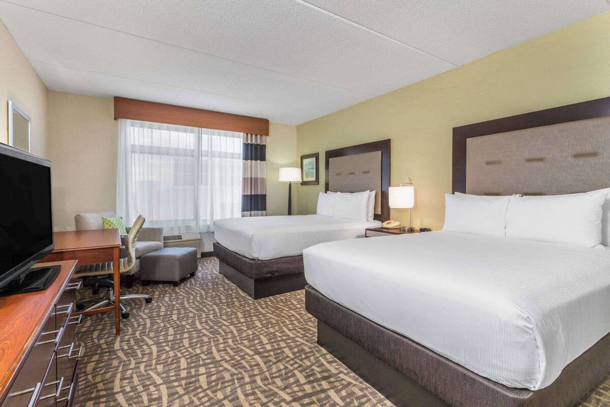 Une chambre d’hôtel avec deux lits, un bureau doté d’un téléviseur à écran plat, une chaise et une moquette à motifs.