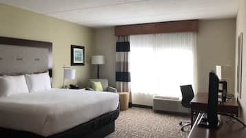 Habitación de hotel con una cama grande, un escritorio con una computadora, una silla, una lámpara y una ventana con cortinas.