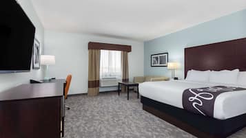 Een hotelkamer met een groot bed, een bureau, een stoel, een televisie en een raam met gordijnen.