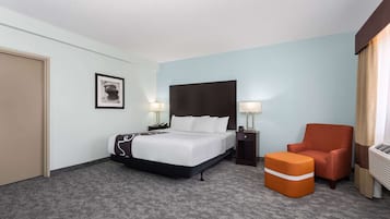 A hotel room with a bed, a chair, a nightstand, and a picture on the wall.