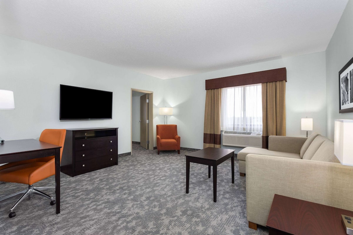 Ein Hotelzimmer mit Flachbildfernseher, Schreibtisch mit Stuhl, Sofa, kleinem Tisch und Lampe.