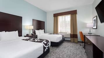 A hotel room with two beds, a desk, a chair, a lamp, and a television.
