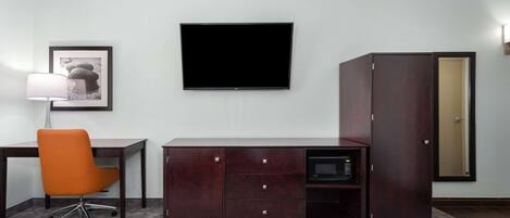 Hotelkamer met een bed, een bureau, een oranje stoel, een televisie, een kledingkast en een magnetron.