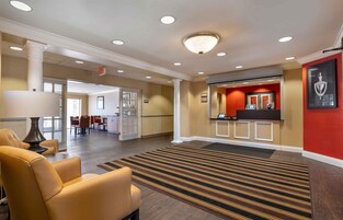 Un hall de hotel con un mostrador de recepción, un área de descanso con sillones y una escalera que sube a otros pisos.