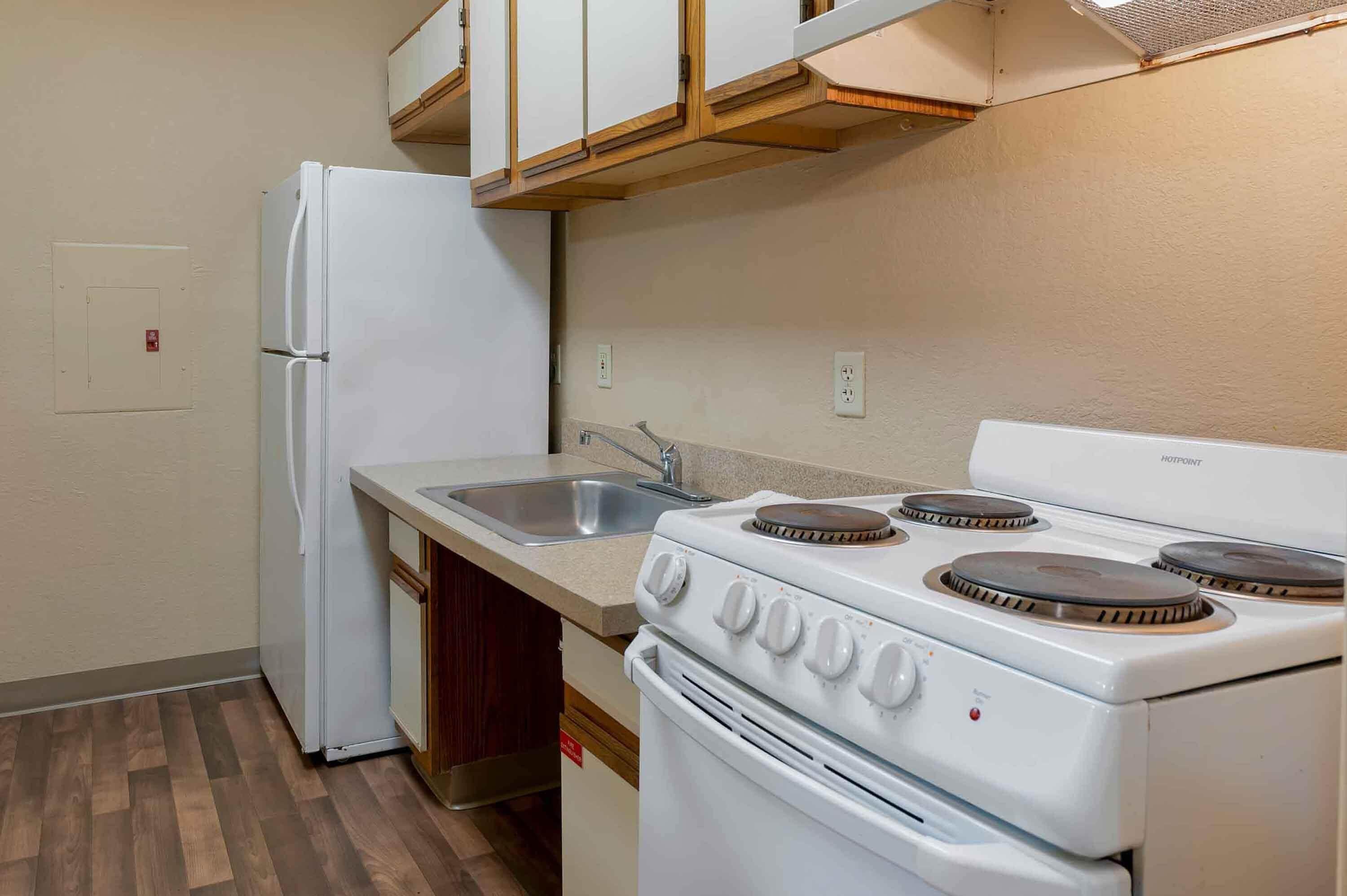 Cocina compacta con refrigerador, estufa, lavamanos y armarios de madera.