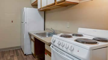 Cocina compacta con refrigerador, estufa, lavamanos y armarios de madera.