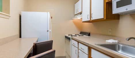 A compact kitchen with white cabinets, a stove, a microwave, and a sink.