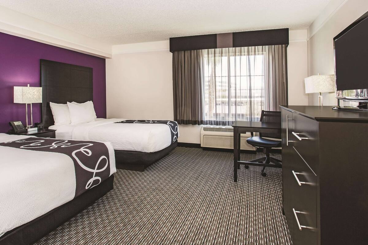 Habitación de hotel con dos camas, un escritorio, una silla, un televisor y una ventana con cortinas.