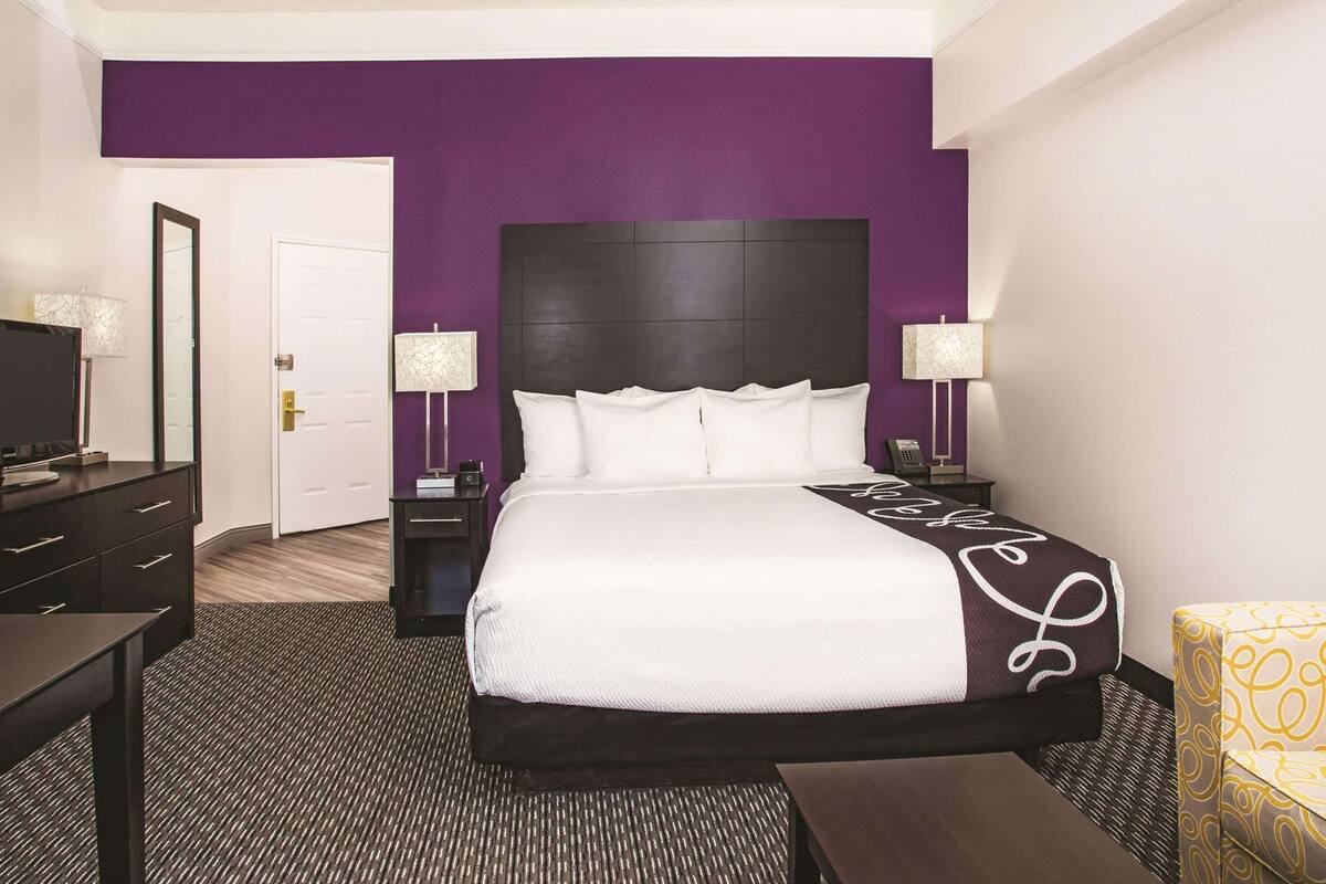 Una habitación de hotel con cama, escritorio, silla, televisor y puerta.