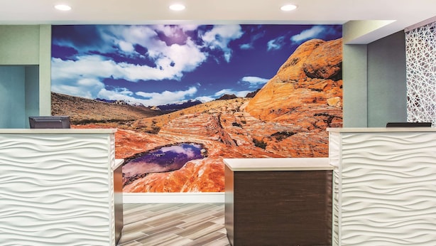 A reception area with a large wall mural of a desert landscape, two reception desks with wavy patterns, and a wooden floor.