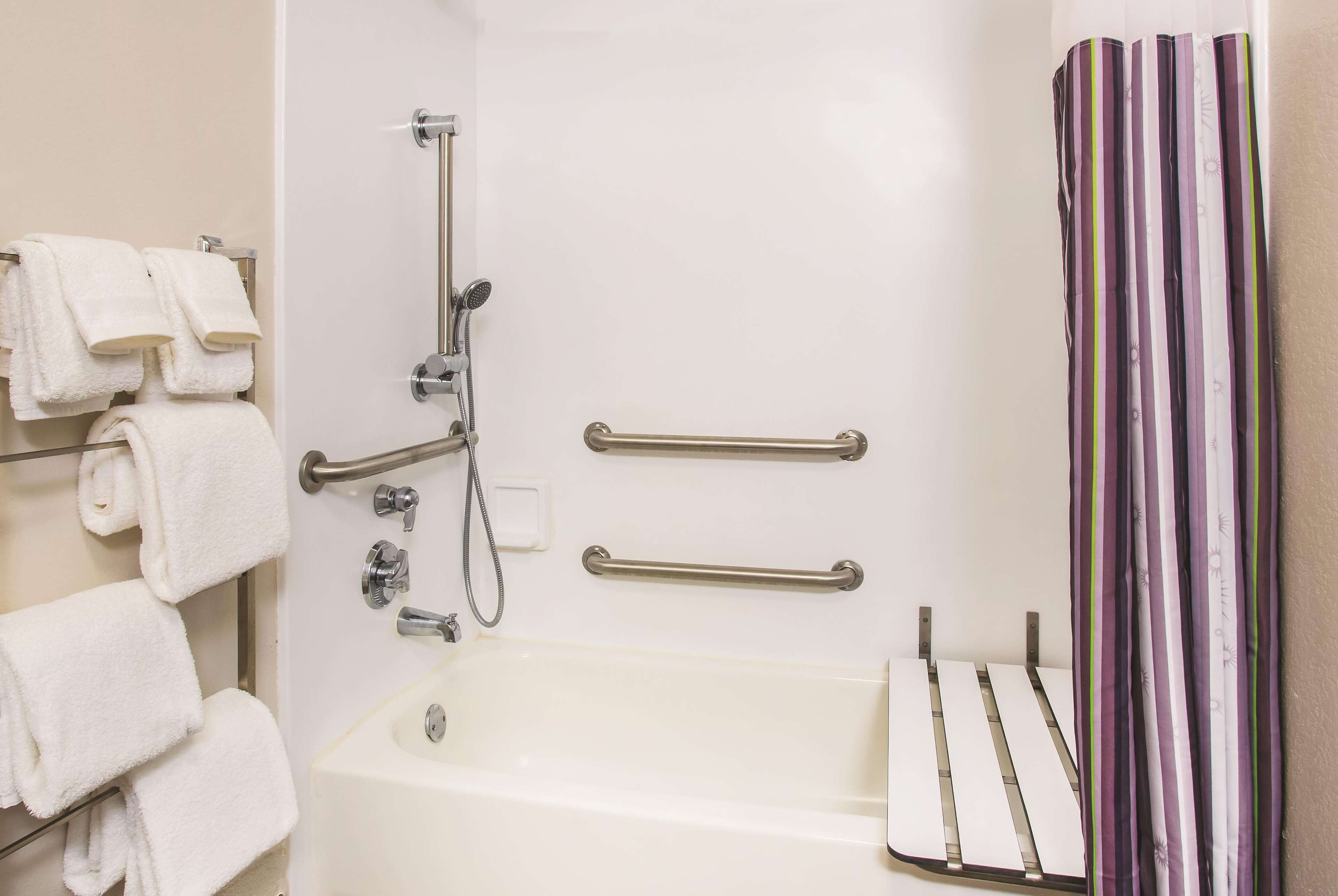 A bathroom with a bathtub, handrails, a showerhead, and a towel rack with towels.