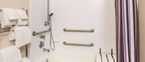 A bathroom with a bathtub, handrails, a showerhead, and a towel rack with towels.