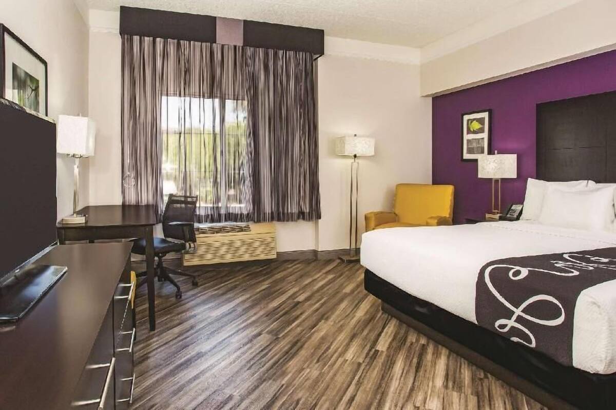 Una habitación de hotel con cama, escritorio, silla y ventana con cortinas.