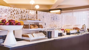 A buffet counter with various food items, including fruits, bread, and pastries.