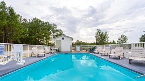 A swimming pool with lounge chairs, a small building, and a fenced area with trees in the background. - Days Inn by Wyndham Lugoff (Lugoff)