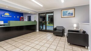 A reception area with a blue wall, a reception desk, a clock, a framed picture, and two black chairs. - Days Inn by Wyndham Lugoff (Lugoff)