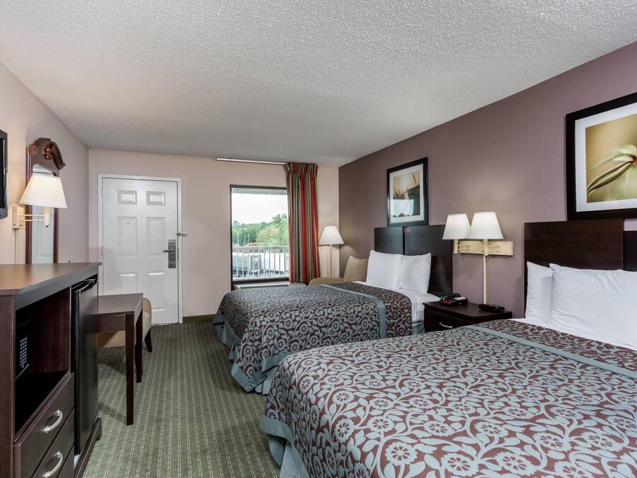 A hotel room with two beds, a desk, a TV, a door, and a window with a view.