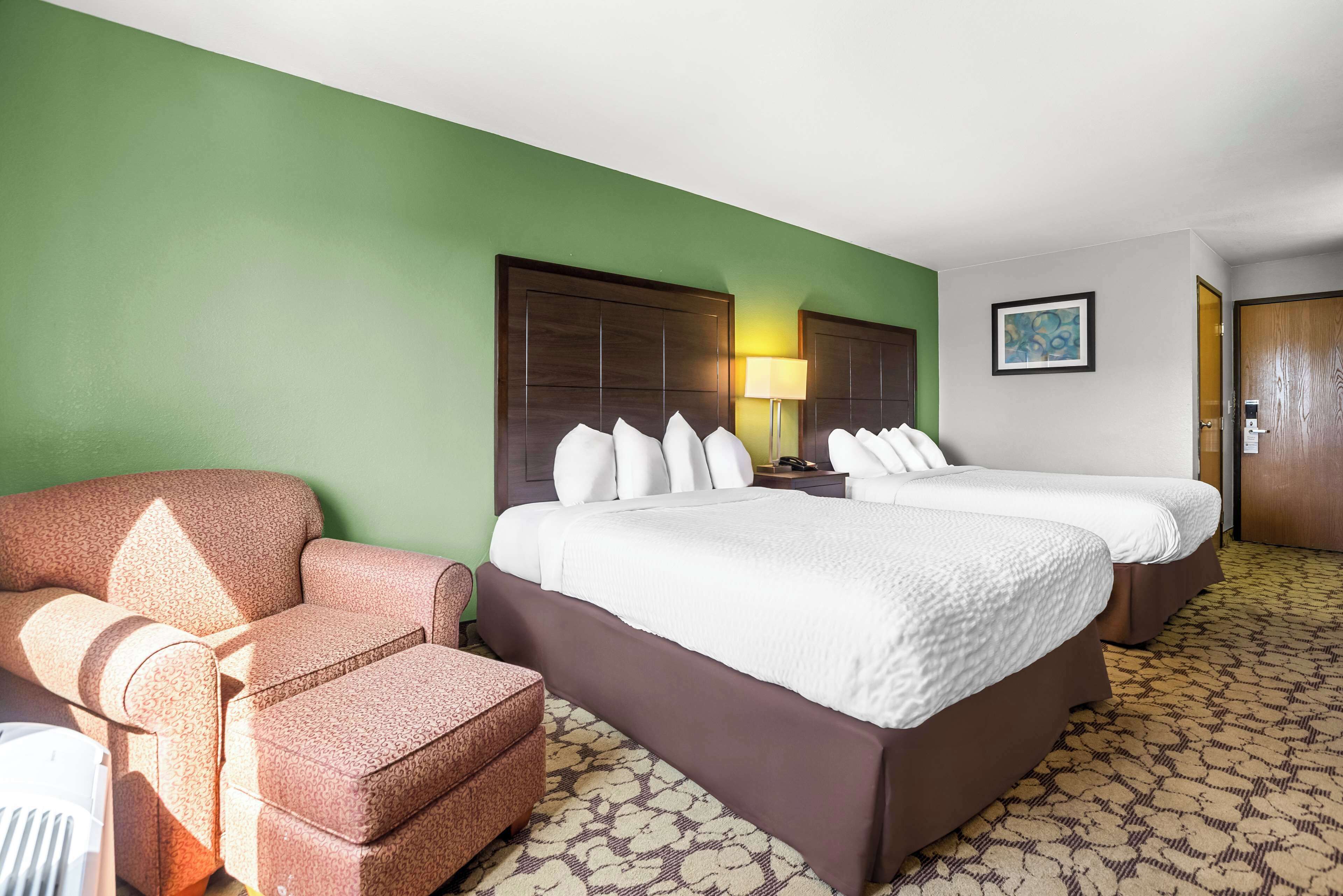 A hotel room with a green wall, two beds with white bedding, a brown sofa, and a patterned carpet.