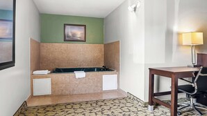 A bathroom with a bathtub, a towel rack, a desk with a chair, and a wall-mounted lamp. - SureStay Plus Hotel by Best Western Bettendorf (Bettendorf)