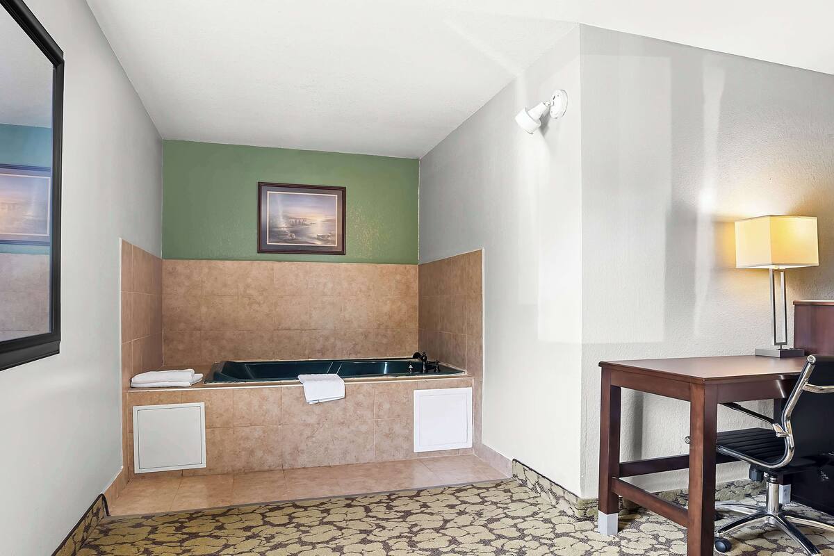 A bathroom with a bathtub, a towel rack, a desk with a chair, and a wall-mounted lamp.