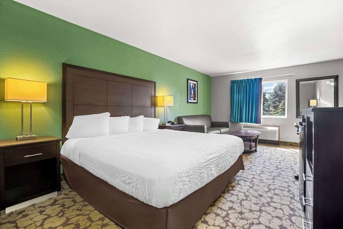 A hotel room with a large bed, two bedside tables with lamps, a desk, a chair, a dresser, and a window with curtains.