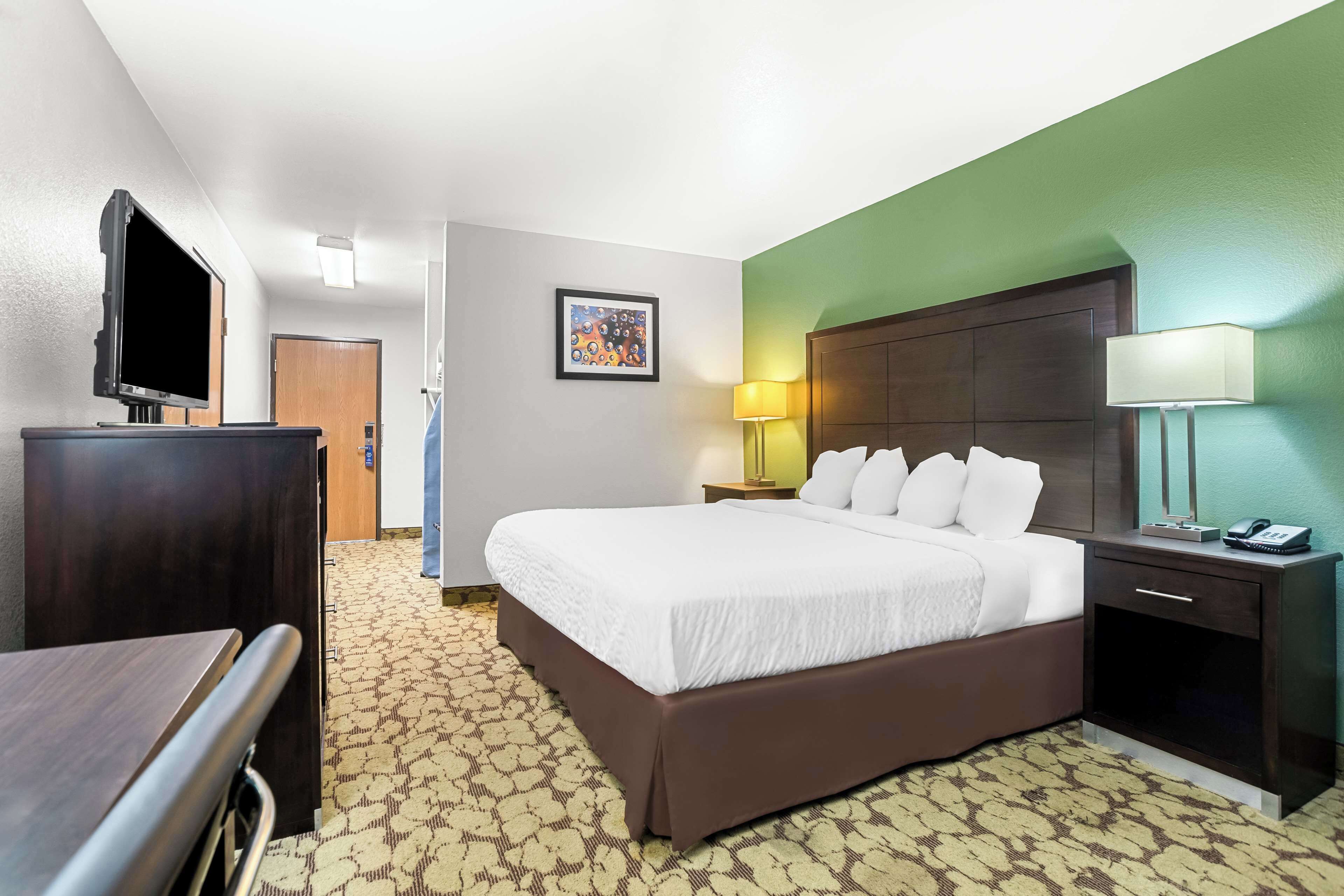 Quarto de hotel com uma cama, uma mesa, uma televisão, uma mesinha de cabeceira com abajur e um quadro pendurado na parede.