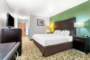 Quarto de hotel com uma cama, uma mesa, uma televisão, uma mesinha de cabeceira com abajur e um quadro pendurado na parede.