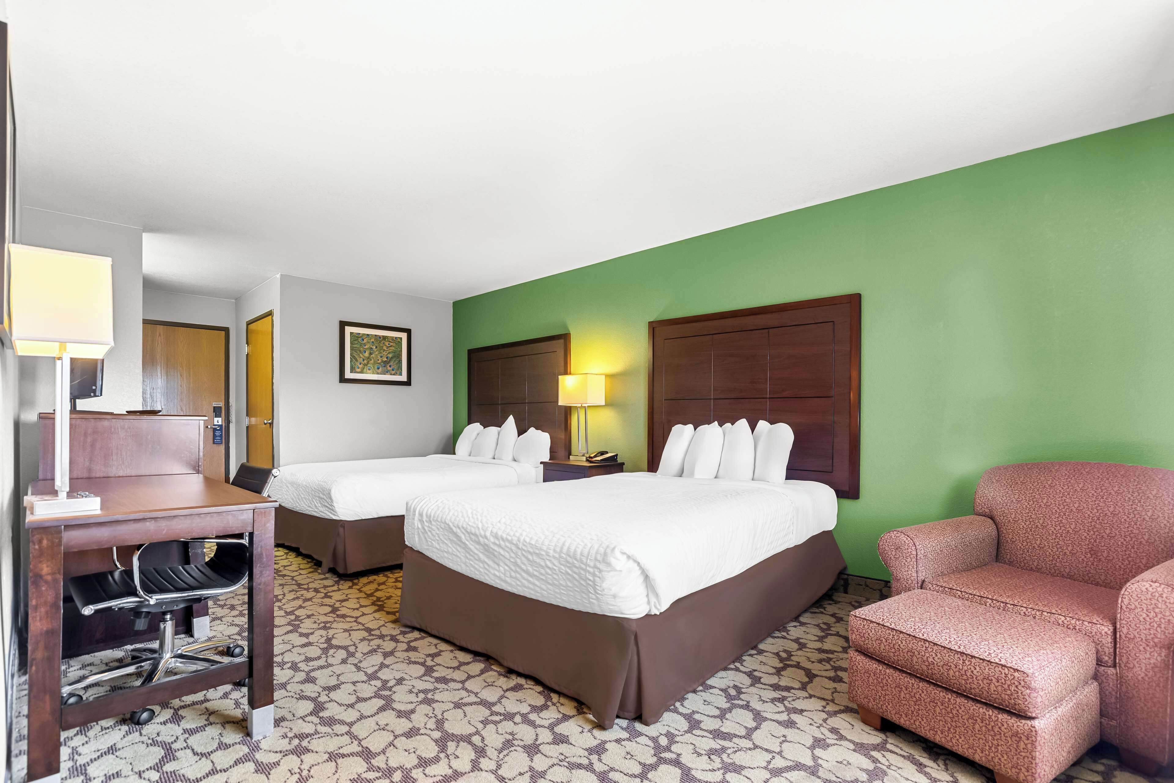 A hotel room with two beds, a desk, a chair, and a green wall.