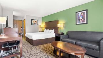 Una habitación de hotel con cama, escritorio con silla, sofá y alfombra estampada.