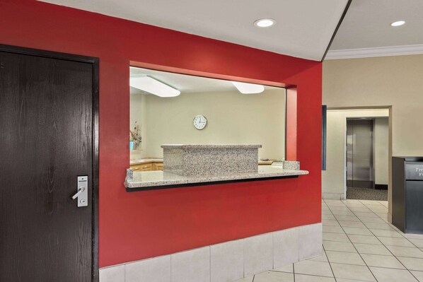 A reception area with a red wall, a granite counter, a clock, and a door.