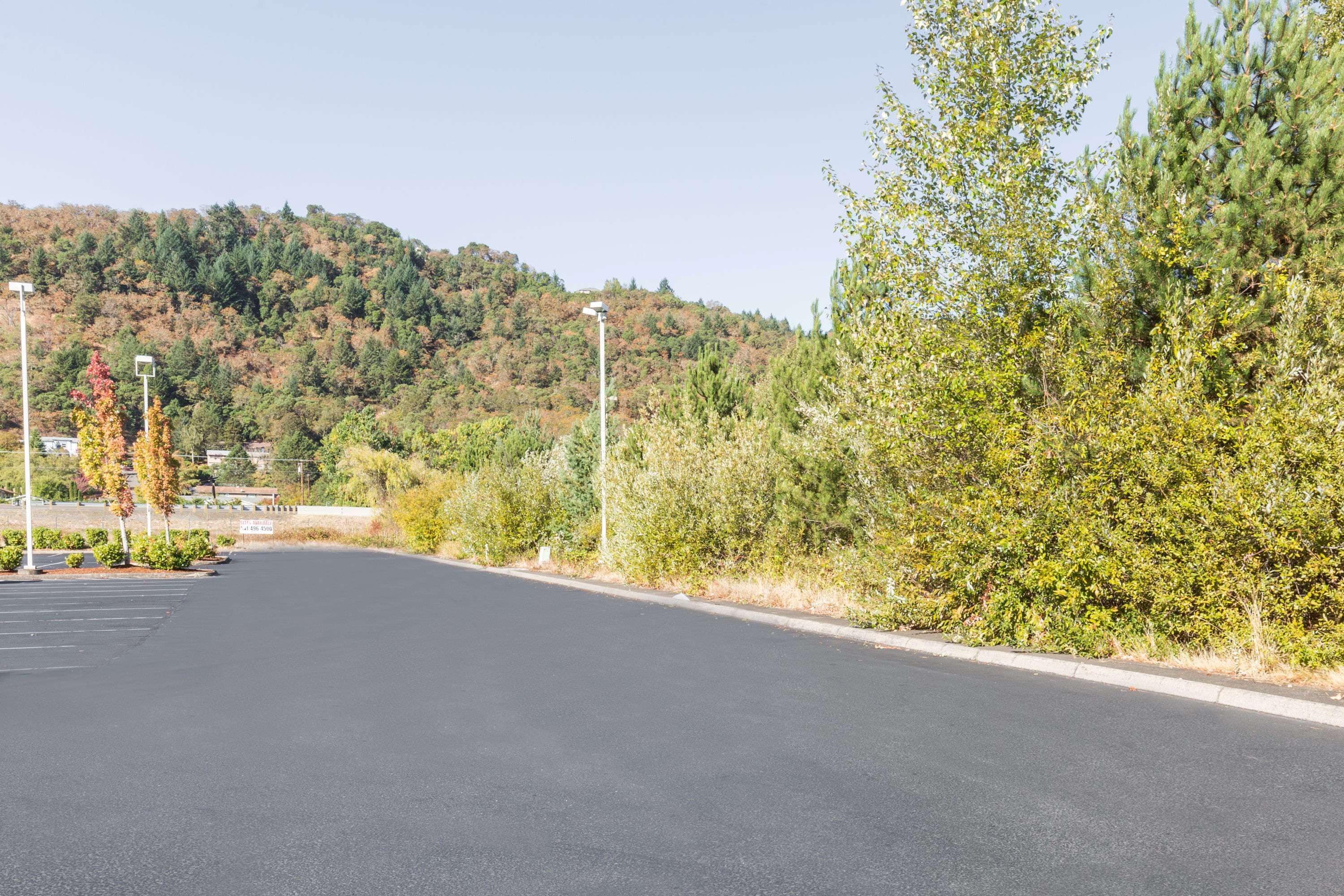 A parking lot with a road leading to a building, surrounded by trees and hills.