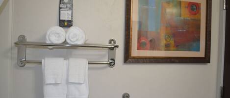 A bathroom with a towel rack holding two rolled towels and a framed abstract painting on the wall.