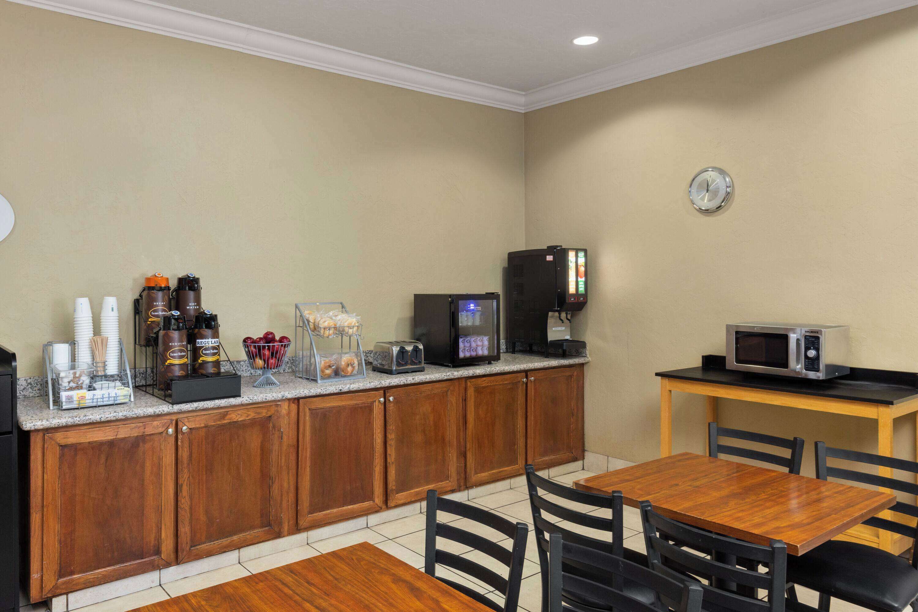 A kitchen with wooden cabinets, a coffee station, a microwave, and a dining table with chairs.
