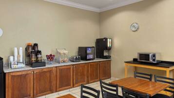 A kitchen with wooden cabinets, a coffee station, a microwave, and a dining table with chairs.