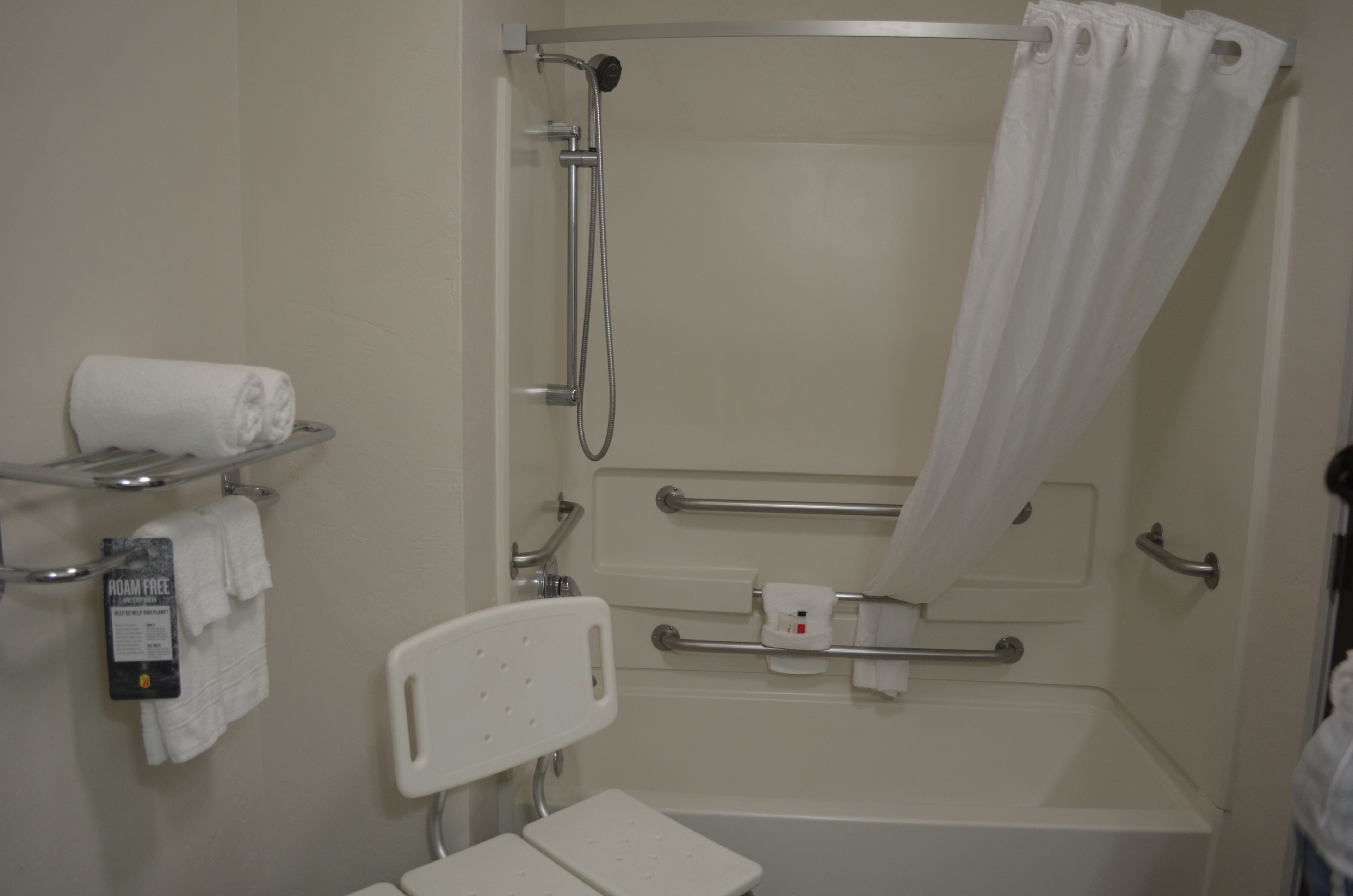 A bathroom with a shower, grab bars, a toilet, and a towel rack.