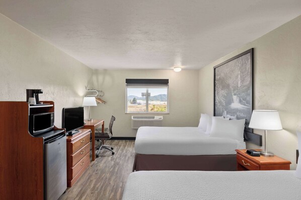 Habitación de hotel con dos camas, un escritorio con computadora, microondas, refrigerador, una silla y ventana con vistas a las montañas.