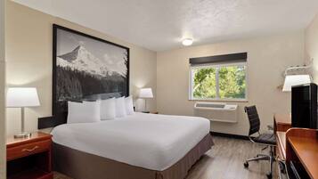 Une chambre d’hôtel avec un grand lit, deux tables de chevet avec des lampes, un bureau avec une chaise, une fenêtre donnant sur un paysage verdoyant et un climatiseur fixé au mur.