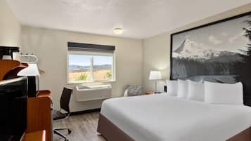 Ein Hotelzimmer mit einem großen Bett, einem Schreibtisch mit Computer, einem Stuhl, einem Fenster mit Aussicht und einem Bild an der Wand.