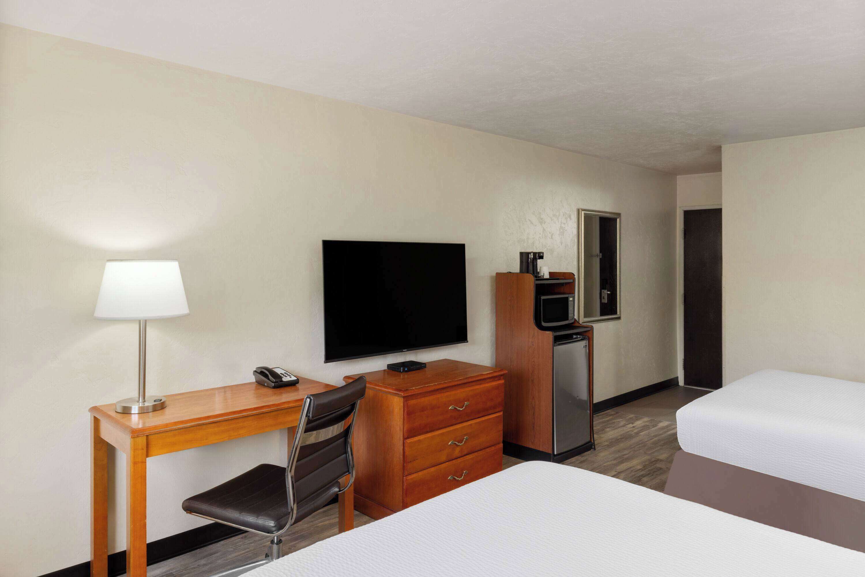 A hotel room with a desk, chair, television, minibar, and two beds.