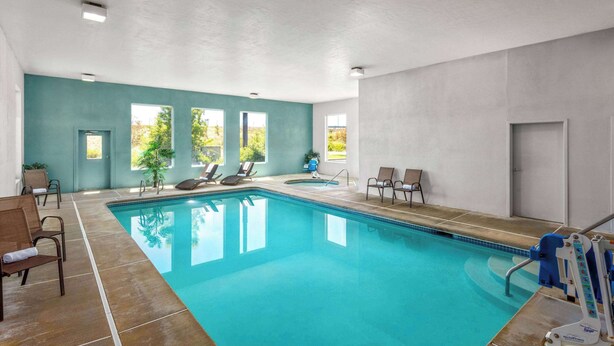 Ein Hallenbad mit klarem, blauem Wasser, umgeben von Liegestühlen und einigen Fenstern.