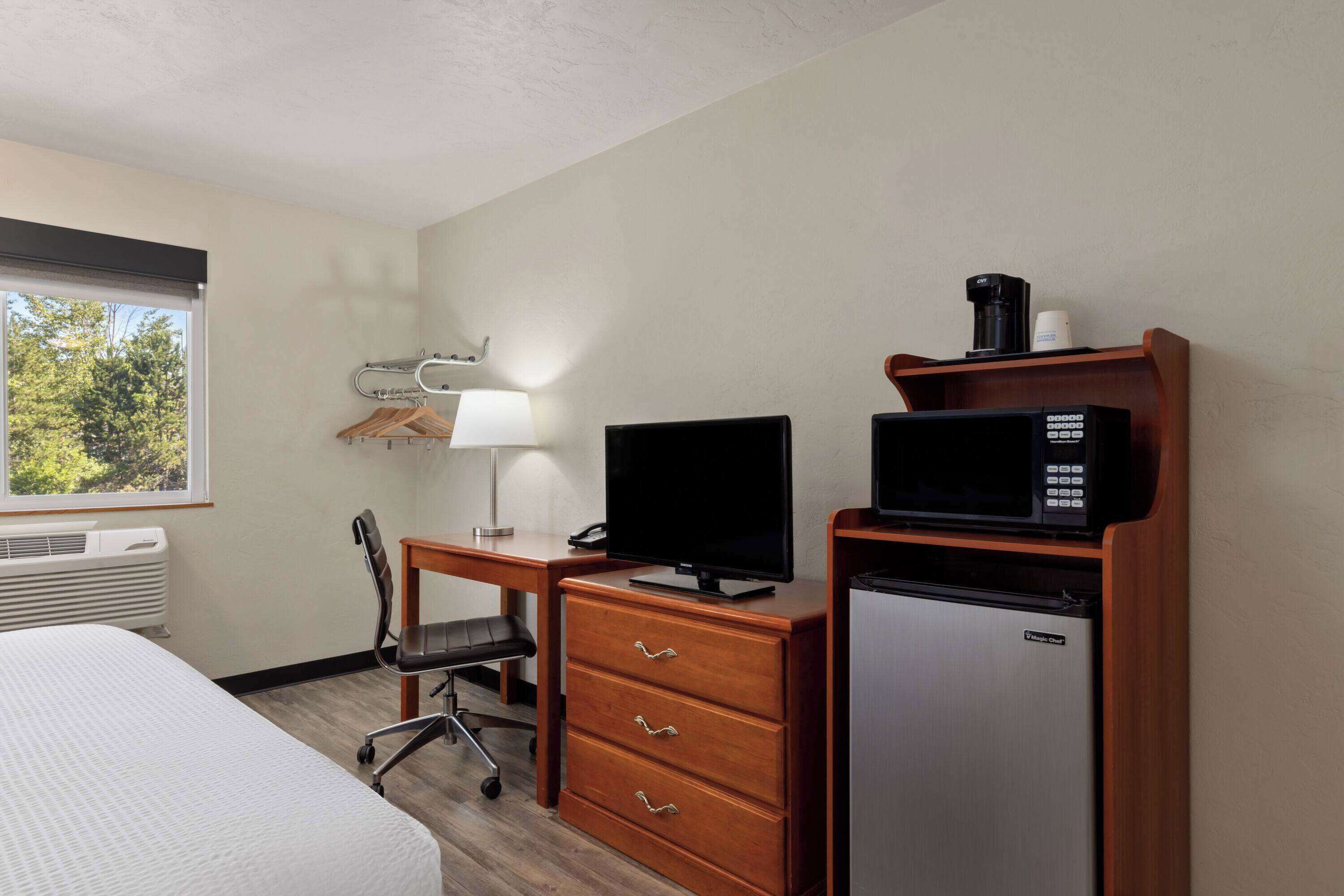 A hotel room with a bed, desk, chair, TV, microwave, and refrigerator.