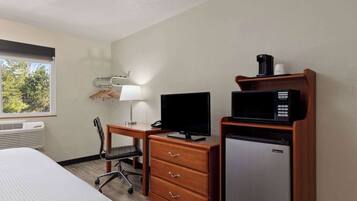 A hotel room with a bed, desk, chair, TV, microwave, and refrigerator.
