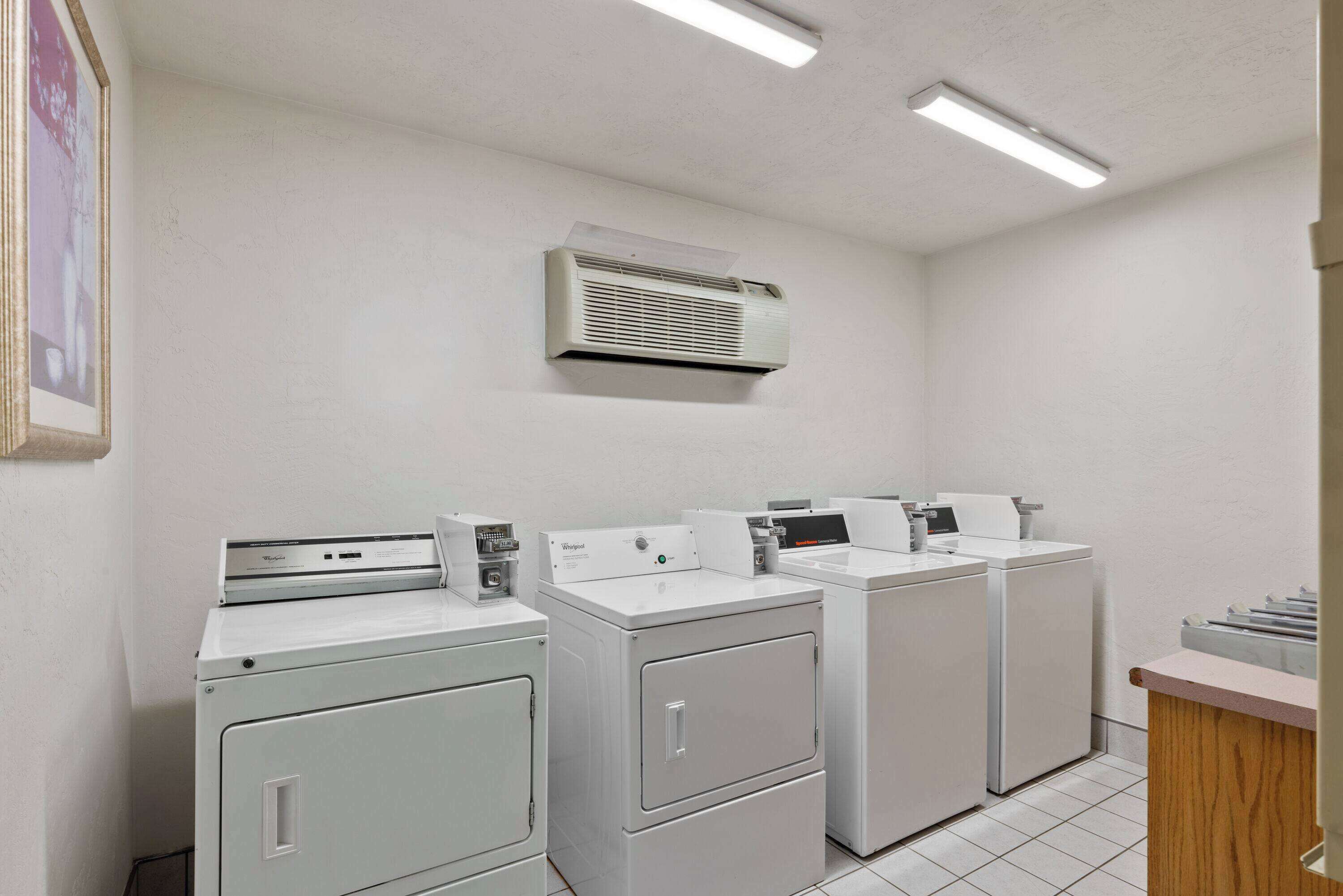 A laundry room with four washers and dryers, an air conditioning unit, and a wooden counter.