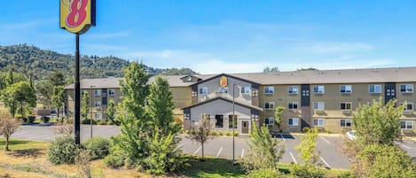 A Super 8 hotel with a parking lot, surrounded by greenery and a mountainous backdrop.