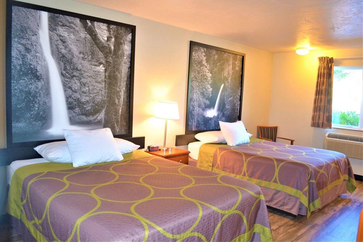 Une chambre d’hôtel avec deux lits, une table de chevet, une lampe et de grandes images encadrées accrochées aux murs.