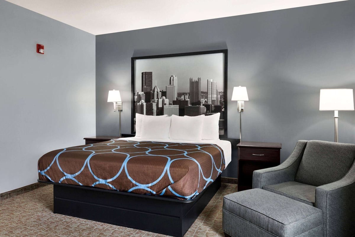 A hotel room with a bed, two bedside lamps, a chair, and a cityscape wall art.