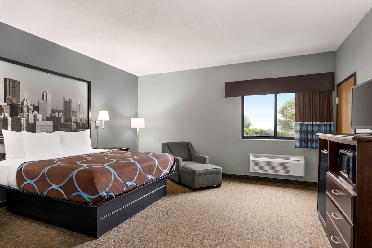 A hotel room with a bed, a chair, a television, and a window with curtains.
